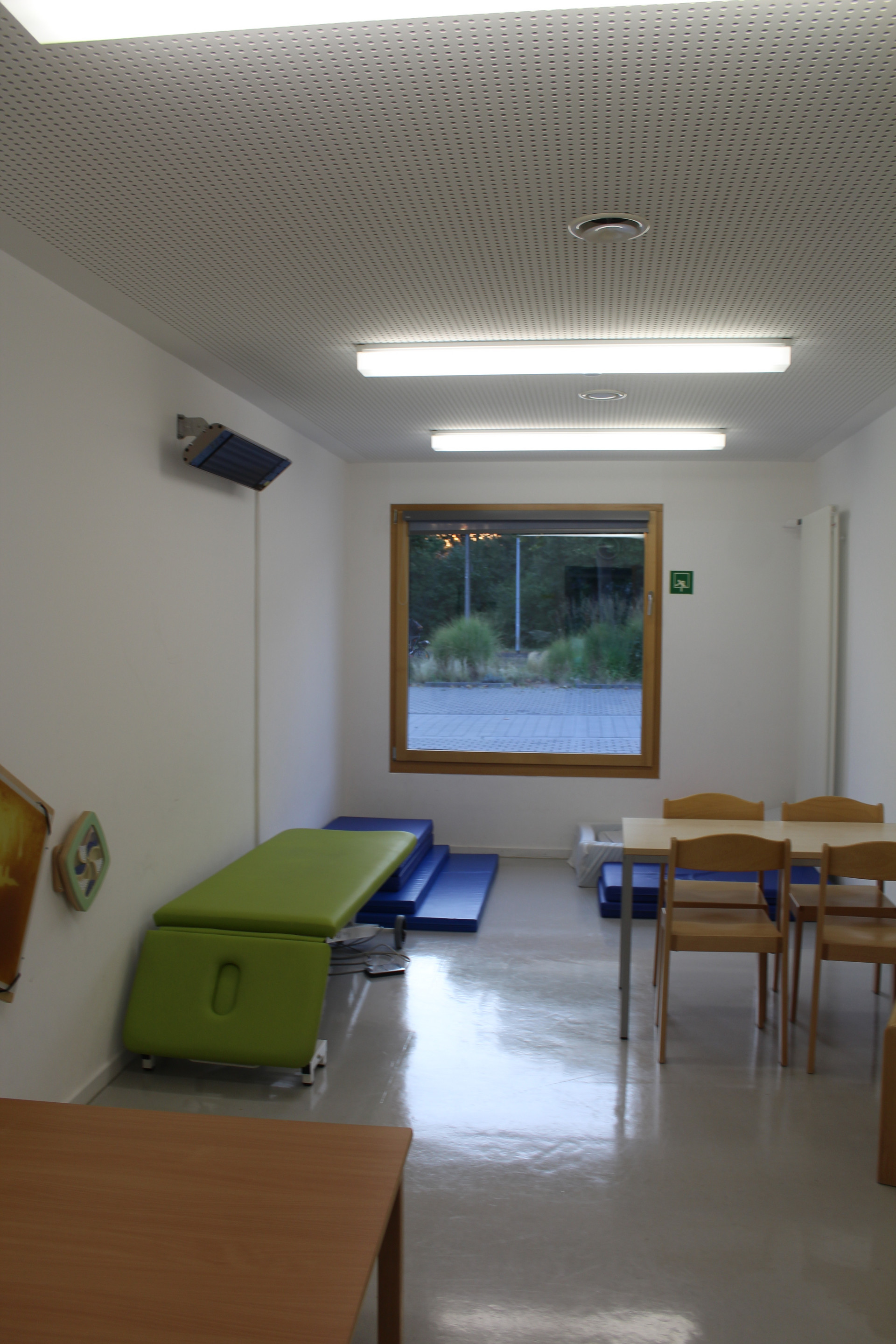 Therapieraum mit Tischen, Stühlen und einer Liege