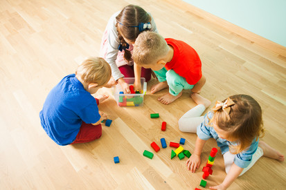 Vier Kinder sitzen auf dem Fußboden und spielen mit Bauklötzen.