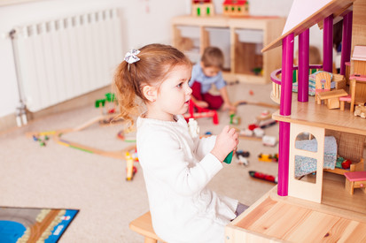 Mädchen spielt mit Puppenhaus.