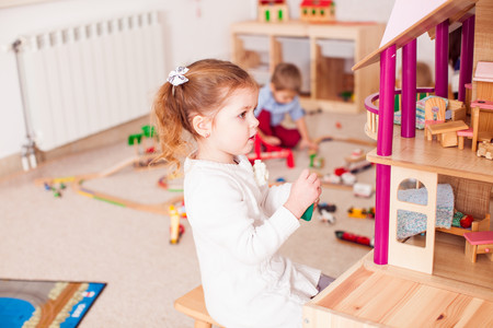 Mädchen spielt mit Puppenhaus.