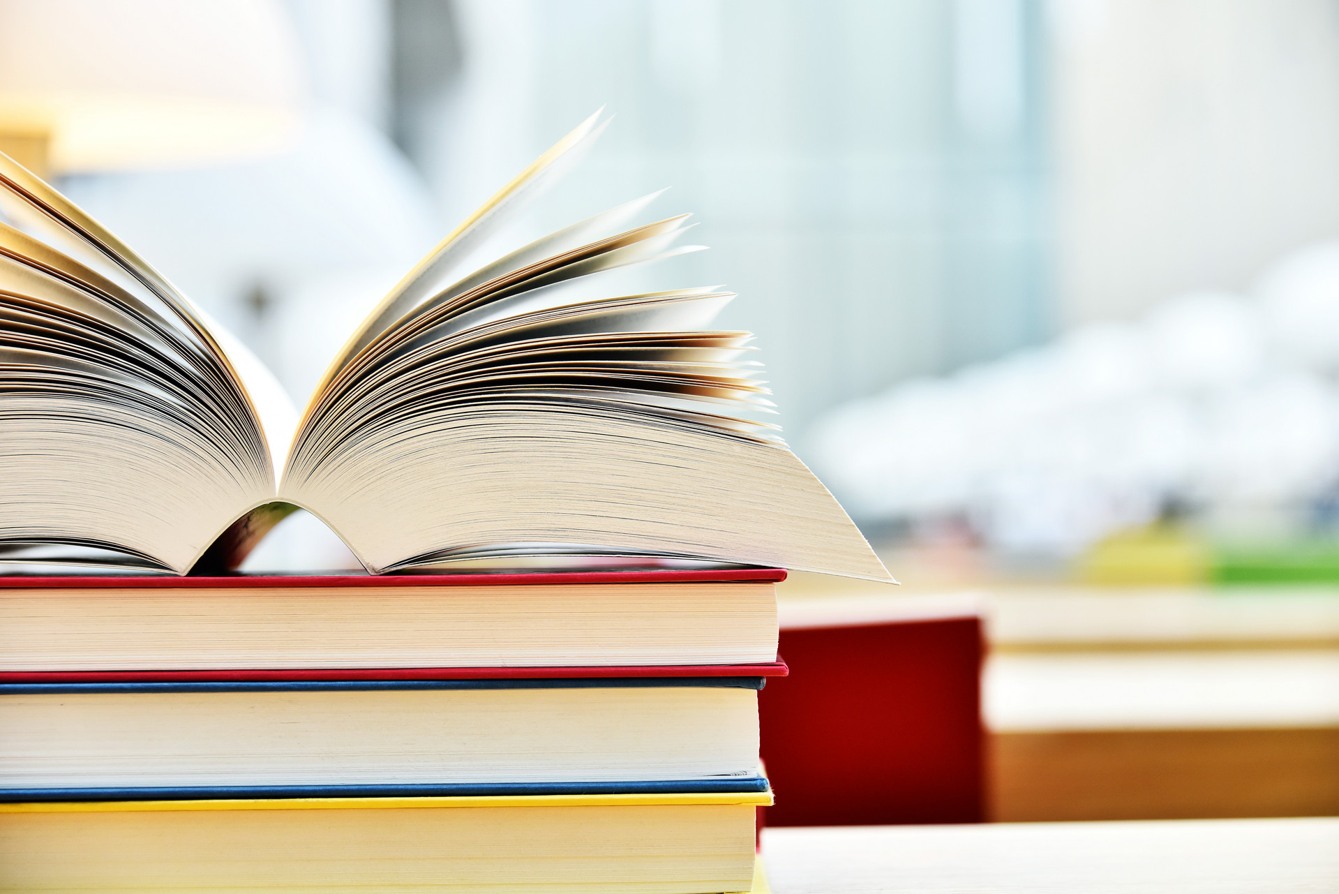 Ein aufgeschlagenes Buch liegt mit dem Rücken auf einem Stapel weiterer Bücher.