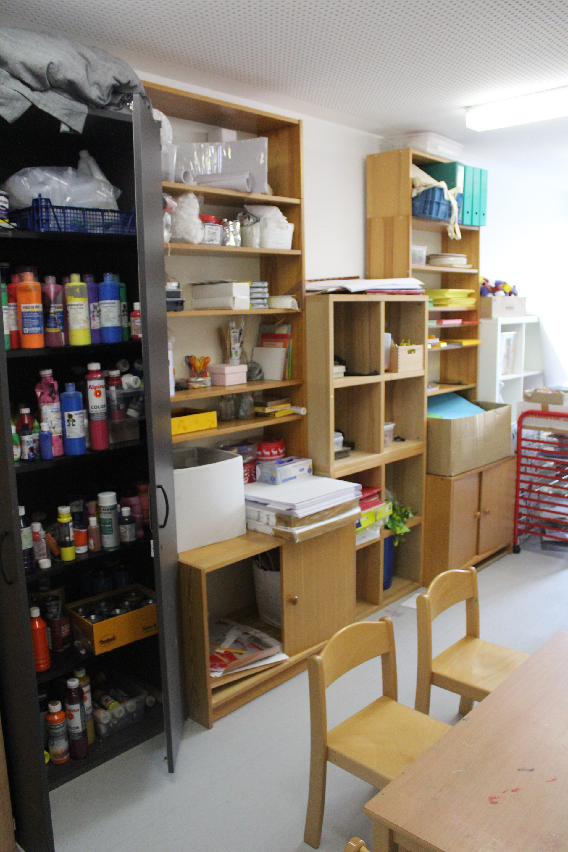 Blick in einen Bastelraum mit bunten Flaschen in einem Regal, einem Tisch und Stühlen