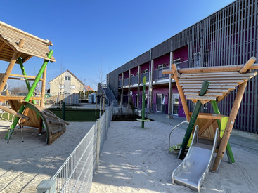 Blick vom Spielplatz mit Klettermöglichkeiten auf das Gebäude