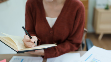 Frau schreibt etwas in ein Notizbuch.